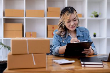 Bir e-ticaret şirketini işleten kadın, onlara göndermeden önce müşterilerin bir listesini kağıda yazıyor. Web sitelerinde ve sosyal medyada bir e-ticaret şirketi işletiyor. Çevrimiçi ürün satma kavramı.