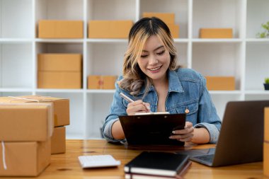 Bir e-ticaret şirketini işleten kadın, onlara göndermeden önce müşterilerin bir listesini kağıda yazıyor. Web sitelerinde ve sosyal medyada bir e-ticaret şirketi işletiyor. Çevrimiçi ürün satma kavramı.