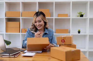 Woman who runs an e-commerce business is writing a list of customers on paper before shipping to them, she runs an e-commerce business on websites and social media. Concept of selling products online.