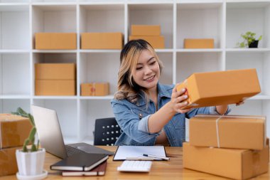 Asyalı bir kadın müşteri kutularını kontrol ediyor, çevrimiçi bir mağazası var, web sitesindeki müşterilerden sipariş alıyor ve özel bir kurye servisi aracılığıyla gönderiyor. Çevrimiçi satış kavramı.