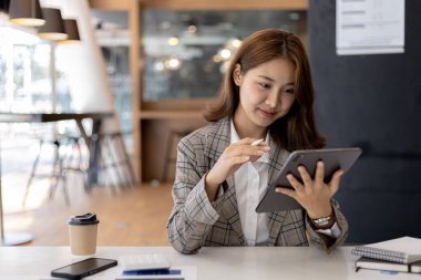 Elinde şirketin mali belgelerini açan tableti tutan bir iş kadını, mali yönetim planını analiz etmek için belgelerdeki bilgileri kontrol ediyor..