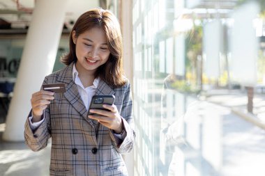 Elinde cep telefonu ve kredi kartı olan bir kadın, akıllı bir telefondan alışveriş yapıyor, mal ve hizmetleri kredi kartıyla ödüyor. Ödeme için kredi kartı kullanma kavramı.