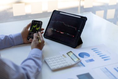 Bir yatırımcı cep telefonları ve tabletlerin hisse tablolarına bakıyor, hisse senedi yatırımcısı, grafikleri analiz ederek hisse senedi ticareti yapıyor ve ticarete girmek için göstergeler kullanıyor. Hisse yatırım fikri.