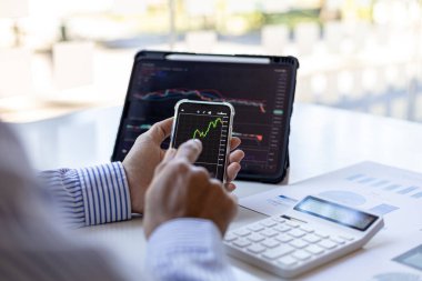 Bir yatırımcı cep telefonları ve tabletlerin hisse tablolarına bakıyor, hisse senedi yatırımcısı, grafikleri analiz ederek hisse senedi ticareti yapıyor ve ticarete girmek için göstergeler kullanıyor. Hisse yatırım fikri.