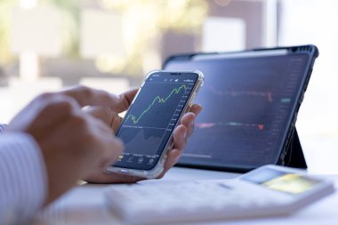 Bir yatırımcı cep telefonları ve tabletlerin hisse tablolarına bakıyor, hisse senedi yatırımcısı, grafikleri analiz ederek hisse senedi ticareti yapıyor ve ticarete girmek için göstergeler kullanıyor. Hisse yatırım fikri.