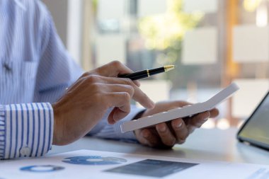 Bir şirketin mali belgelerindeki rakamları hesaplamak için hesap makinesi kullanan bir işadamı, şirketin nasıl büyüyeceğini planlamak için tarihsel finansal verileri analiz ediyor. Mali konsept.