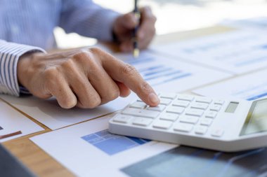 Businessman using a calculator to calculate numbers on a company's financial documents, he is analyzing historical financial data to plan how to grow the company. Financial concept.