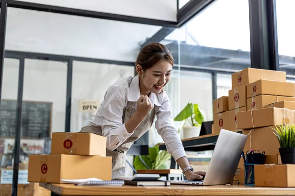 A beautiful Asian business owner opens an online store, she is checking orders from customers via laptop, sending goods through a courier company, concept of a woman opening an online business.