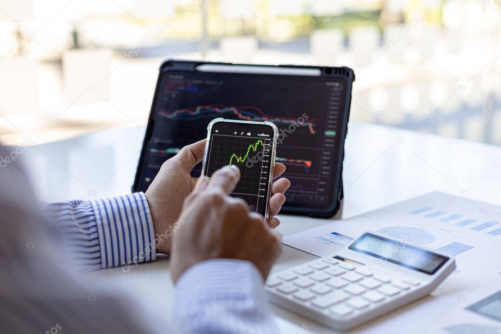 An investor is looking at stock charts on mobile phones and tablets, he is a stock investor, he trades stocks by analyzing the charts and using indicators to enter trades. Stock investment idea.