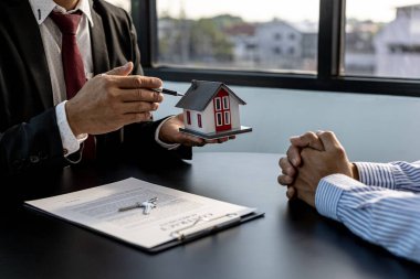 Projedeki emlak satıcısı, inşaattaki yapı ve malzemeleri tanımlamak için küçük bir evin modeline işaret ediyor. Konut ve gayrimenkul satma kavramı.