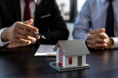Projedeki emlak satıcısı, inşaattaki yapı ve malzemeleri tanımlamak için küçük bir evin modeline işaret ediyor. Konut ve gayrimenkul satma kavramı.