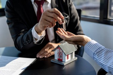 Bir ev kiralama şirketi çalışanı kira sözleşmesi imzalamayı kabul eden bir müşteriye kira sözleşmesinin detaylarını ve şartlarını açıklayan ev anahtarlarını teslim ediyor. Ev ve gayrimenkul kiralama fikirleri.