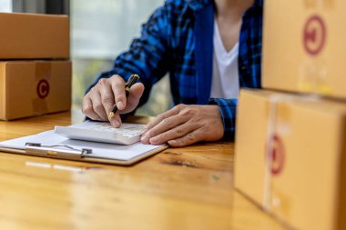 Bir adam sipariş miktarını hesaplamak için hesap makinesine basıyor, bir online mağazası var, özel bir nakliye şirketi aracılığıyla paketleyip gönderiyor. Çevrimiçi satış ve online alışveriş kavramları.