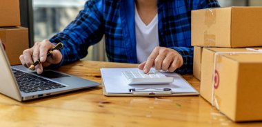 Bir adam sipariş miktarını hesaplamak için hesap makinesine basıyor, bir online mağazası var, özel bir nakliye şirketi aracılığıyla paketleyip gönderiyor. Çevrimiçi satış ve online alışveriş kavramları.