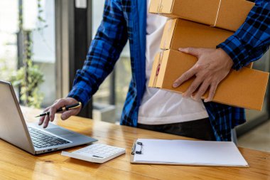 Paket kutuları tutan ve tabletten sipariş alan Asyalı bir adam, bir online mağazası var, özel bir nakliye şirketi aracılığıyla paketleyip gönderiyor. Çevrimiçi satış ve online alışveriş kavramları.