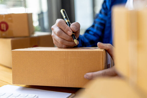 Asian person writing customer's shipping information on parcel box, He owns an online store, He ships products to customers through a private courier company. Online selling concept.