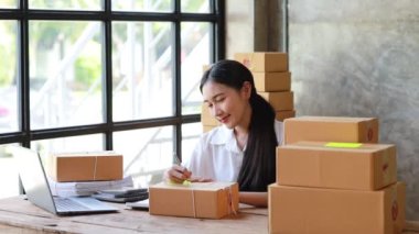 Bir e-ticaret şirketini işleten kadın, onlara göndermeden önce müşterilerin bir listesini kağıda yazıyor. Web sitelerinde ve sosyal medyada bir e-ticaret şirketi işletiyor. Çevrimiçi ürün satma kavramı.