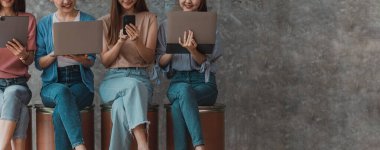 Asyalı kadın şirket çalışanları ellerinde elektronik iletişim cihazları ve dizüstü bilgisayarlarıyla sıra sıra otururlar. Yeni jenerasyon ve yeni konsept şirketi ile yeni bir şirket kurmak için çalışma kavramı.