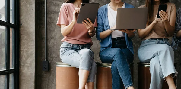 Asyalı kadın şirket çalışanları ellerinde elektronik iletişim cihazları ve dizüstü bilgisayarlarıyla sıra sıra otururlar. Yeni jenerasyon ve yeni konsept şirketi ile yeni bir şirket kurmak için çalışma kavramı.