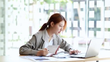 Güzel bir Asyalı kadın bir şirkette özel bir ofiste oturuyor, bir şirket işleten bir iş kadını, büyümek için bir iş geliştirmeyi planlıyor. İş idaresi konsepti. 4K.