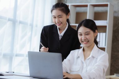 Girişim şirketinin atmosferinde, iki kadın çalışan, satışları artırmak ve yöneticilere raporlar hazırlamak için özetler ve pazarlama planları üzerinde çalışmak üzere fikir alışverişinde bulunuyorlar..