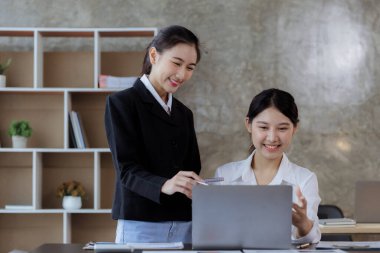 Girişim şirketinin atmosferinde, iki kadın çalışan, satışları artırmak ve yöneticilere raporlar hazırlamak için özetler ve pazarlama planları üzerinde çalışmak üzere fikir alışverişinde bulunuyorlar..