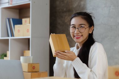 A beautiful Asian business owner opens an online store, she is checking orders from customers, sending goods through a courier company, concept of a woman opening an online business.
