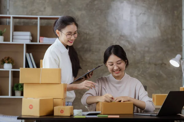 A beautiful Asian business owner opens an online store, she is checking orders from customers, sending goods through a courier company, concept of a woman opening an online business.