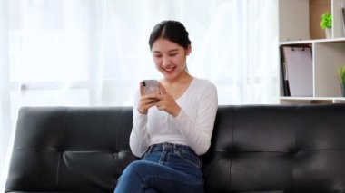 Oturma odasındaki kanepede akıllı telefon oynayan bir kadın, yoğun bir iş gününden sonra hafta sonları dinleniyor, internetten alışveriş yapıyor ve kredi kartıyla ödüyor. Kredi kartı ödeme kavramı.