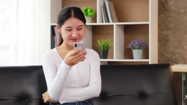 A woman playing smartphone on the sofa in her home living room, she is relaxing on weekends after a hard day's work, she is shopping online and paying by credit card. Credit card payment concept.