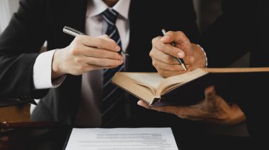 İki avukat, ortak bir kovuşturma sözleşmesi hazırlamak ve müvekkillerini savunmak için davanın detaylarına bakmak amacıyla büyük bir hukuk kitabı okuyorlar. Hukuk ve adalet kavramı.