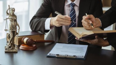 İki avukat, ortak bir kovuşturma sözleşmesi hazırlamak ve müvekkillerini savunmak için davanın detaylarına bakmak amacıyla büyük bir hukuk kitabı okuyorlar. Hukuk ve adalet kavramı.