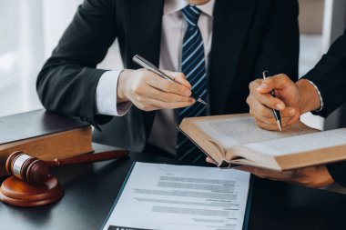 İki avukat, ortak bir kovuşturma sözleşmesi hazırlamak ve müvekkillerini savunmak için davanın detaylarına bakmak amacıyla büyük bir hukuk kitabı okuyorlar. Hukuk ve adalet kavramı.