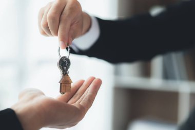 Bir ev kiralama şirketi çalışanı kira sözleşmesi imzalamayı kabul eden bir müşteriye kira sözleşmesinin detaylarını ve şartlarını açıklayan ev anahtarlarını teslim ediyor. Ev ve gayrimenkul kiralama fikirleri.