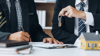 Bir ev kiralama şirketi çalışanı kira sözleşmesi imzalamayı kabul eden bir müşteriye kira sözleşmesinin detaylarını ve şartlarını açıklayan ev anahtarlarını teslim ediyor. Ev ve gayrimenkul kiralama fikirleri.