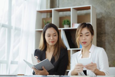 Girişim şirketinin atmosferinde, iki kadın çalışan, satışları artırmak ve yöneticilere raporlar hazırlamak için özetler ve pazarlama planları üzerinde çalışmak üzere fikir alışverişinde bulunuyorlar..