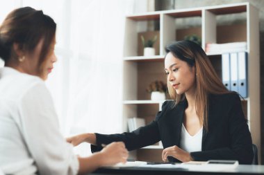 Girişim şirketinin atmosferinde, iki kadın çalışan, satışları artırmak ve yöneticilere raporlar hazırlamak için özetler ve pazarlama planları üzerinde çalışmak üzere fikir alışverişinde bulunuyorlar..