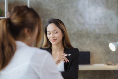 Girişim şirketinin atmosferinde, iki kadın çalışan, satışları artırmak ve yöneticilere raporlar hazırlamak için özetler ve pazarlama planları üzerinde çalışmak üzere fikir alışverişinde bulunuyorlar..