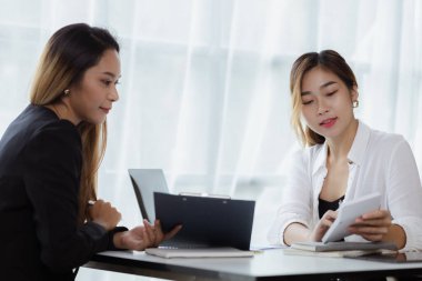 Girişim şirketinin atmosferinde, iki kadın çalışan, satışları artırmak ve yöneticilere raporlar hazırlamak için özetler ve pazarlama planları üzerinde çalışmak üzere fikir alışverişinde bulunuyorlar..