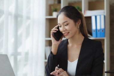 Asian woman talking on the phone, she is a salesperson in a startup company, she is calling customers to sell products and promotions. Concept of selling products through telephone channels. 