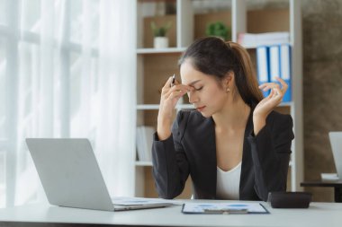 Beautiful Asian woman working in an office, she is a businesswoman who owns a company, she has a headache due to long and large paperwork leaving her tired and dizzy. The concept of sickness from work