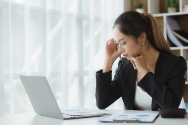 Beautiful Asian woman working in an office, she is a businesswoman who owns a company, she has a headache due to long and large paperwork leaving her tired and dizzy. The concept of sickness from work