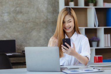 Kadın el kol hareketi yapıyor ve cep telefonu ekranına bakıyor, iş kadını aylık satışları kontrol ediyor ve satış planlanan hedeflere ulaşırken mutluymuş gibi davranıyor. Satış yönetimi kavramı.