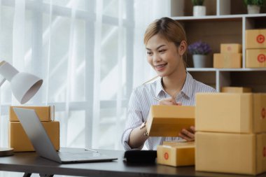 Bir e-ticaret şirketini işleten kadın, onlara göndermeden önce müşterilerin bir listesini kağıda yazıyor. Web sitelerinde ve sosyal medyada bir e-ticaret şirketi işletiyor. Çevrimiçi ürün satma kavramı.