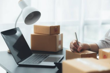 Bir e-ticaret şirketini işleten kadın, onlara göndermeden önce müşterilerin bir listesini kağıda yazıyor. Web sitelerinde ve sosyal medyada bir e-ticaret şirketi işletiyor. Çevrimiçi ürün satma kavramı.