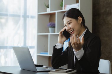 Asian woman talking on the phone, she is a salesperson in a startup company, she is calling customers to sell products and promotions. Concept of selling products through telephone channels.