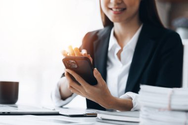 Businesswoman looking at financial information from a mobile phone, she is checking company financial documents, she is a female executive of a startup company. Concept of financial management.