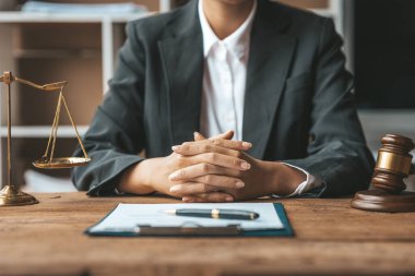 A woman lawyer sits in the office of her law firm, on a table with a scale of justice and a hammer laying down, she is an attorney serving his client. Lawyer concepts and lawful justice.