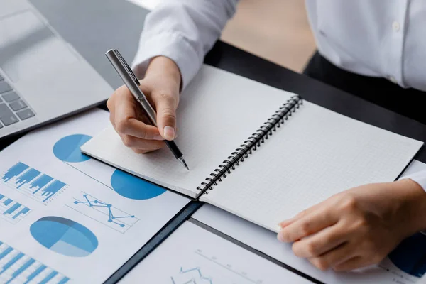 A businesswoman is taking notes in a notebook, she checks company financial documents and she takes corrective reports to the finance manager for correction. Finance concept.