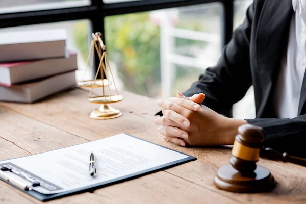 A woman lawyer sits in the office of her law firm, on a table with a scale of justice and a hammer laying down, she is an attorney serving his client. Lawyer concepts and lawful justice.